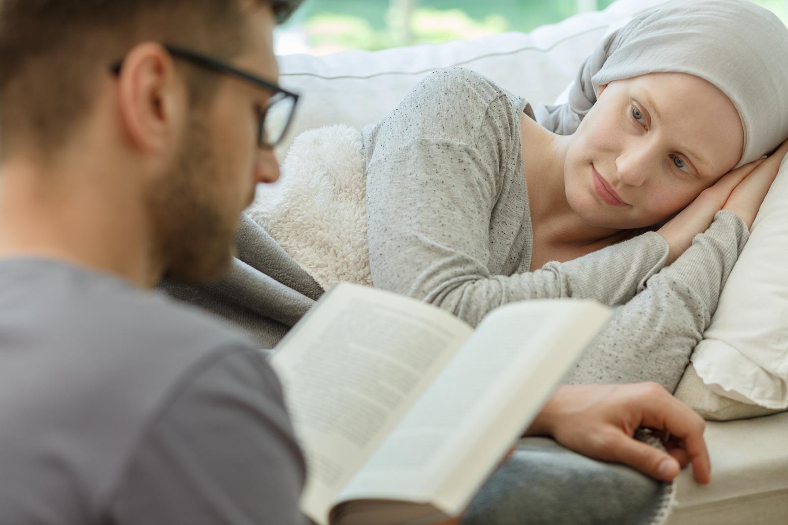 A man reads to a woman who is laying on a couch.